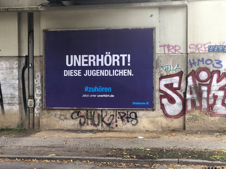 "Unerhört! Diese Jugendlichen. der Diakonie-Kampagne auf einer Wand mit Graffiti.